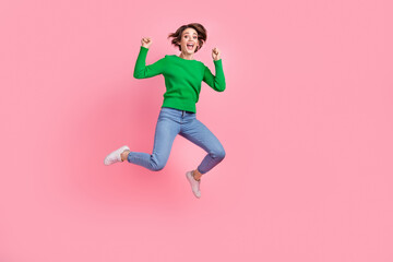 Full length photo of pretty lucky girl dressed green sweater jumping high rising fists empty space isolated pink color background