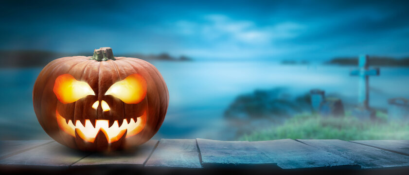 The spooky haunted evil glowing eyes of Jack O' Lanterns, halloween pumpkin, on the right of a wooden bench on a scary halloween night with an ocean background