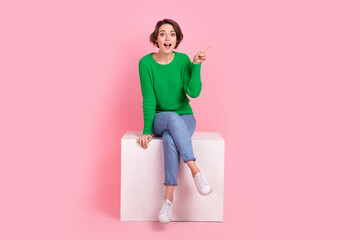 Full length photo of impressed lovely girl wear stylish clothes sitting podium arm direct empty space isolated on pink color background