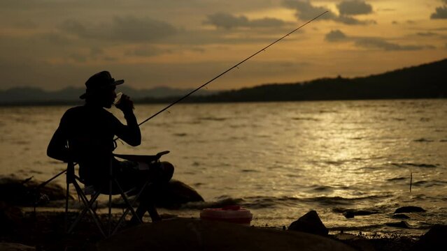 Silhouette of fishermen alone in a boat reeling up a fishing pole in a sunset lake,man recreation with fishing rod outdoor catching lifestyle fish at sunset