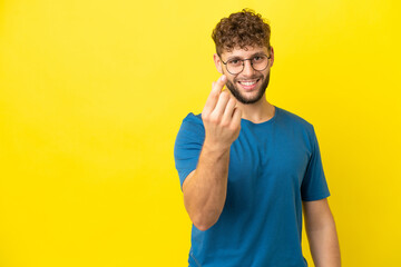 Young handsome caucasian man isolated on yellow background making money gesture