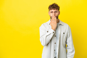 Young handsome caucasian man isolated on yellow background covering mouth with hand