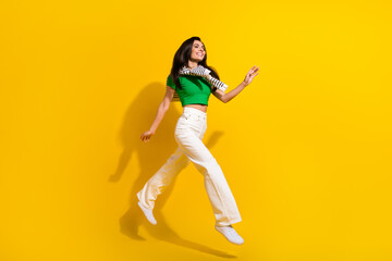 Fototapeta na wymiar Full length photo of cute pretty girl dressed green t-shirt running fast jumping high isolated yellow color background