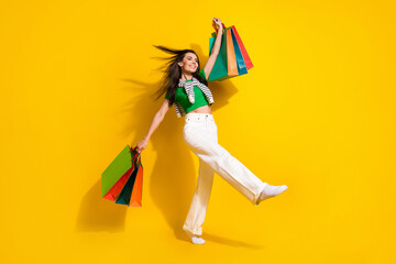 Full length photo of adorable excited lady wear green t-shirt walking rising shoppers isolated yellow color background