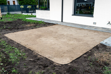 Rolling yellow sand with a steel roller for a garden pool, empty square visible.