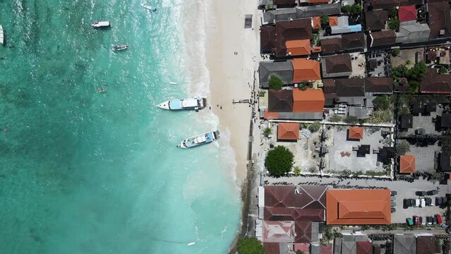 Aerial shoreline view of jetty at Jungut Batu Village in Nusa Lembongan with tourist speedboat anchored on the beach. Travel destinations close to Bali island, Indonesia. 4K drone footage video