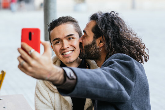 Man giving a kiss on the cheek to his boyfriend sitting in a restaurant.