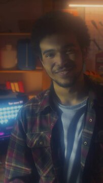 Vertical portrait of young Middle Eastern man standing in garage office finishing phone call then looking at camera, 90s aestheticsVertical portrait of young Middle Eastern man standing in garage offi