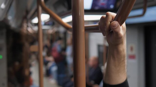 Close-up of a man holding on to a handrail in a subway car. A train passenger holds onto a handrail while the train is moving underground.