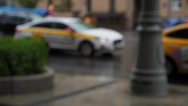 A blurry image of a traffic jam in the city during the rain, passers-by are walking in the foreground. A taxi is driving slowly in a traffic jam in the rain.