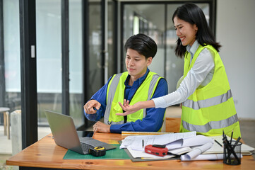 Obraz premium A smart male engineer is discussing a building blueprint on the desktop with his female colleague