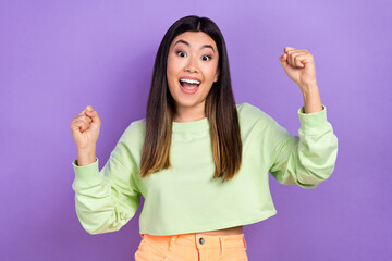 Photo of cute lucky girl dressed green sweatshirt rising fists yelling isolated violet color background