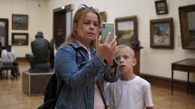 Close-up of a mother and son taking a selfie in an art gallery. A family of tourists visits an art gallery and take pictures on their phone.