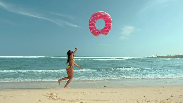 Beautiful young woman in yellow bikini with pink donut swim ring in transparent sea at sunny day in summer. Tropical landscape. Sexy back of slim girl, clear water, blue sky