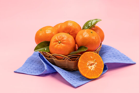 Fresh tangerines in a basket on a pink background.