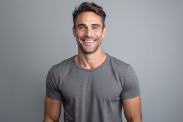 Portrait of a handsome young man smiling and looking at camera on grey background - obrazy, fototapety, plakaty