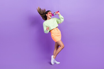 Full size photo of satisfied cute woman dressed green shirt stylish skirt sing pop song in microphone isolated on purple color background