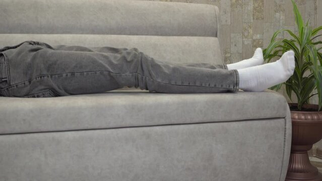 lie down on the couch to rest,the student lies down on the sofa in white socks and jeans