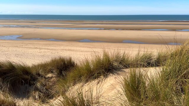 Wide empty beach in North West of England, elevated view from grassy sand dunes towards Irish Sea on a beautiful sunny day.