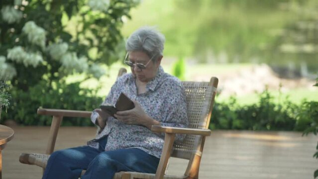 asian old elder senior woman elderly using social media on mobile smart phone cellphone in garden. mature retirement lifestyle