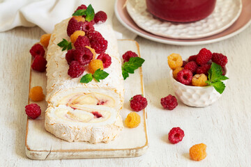 Meringue roll with butter cream and raspberry curd, decorated with berries on a light background.