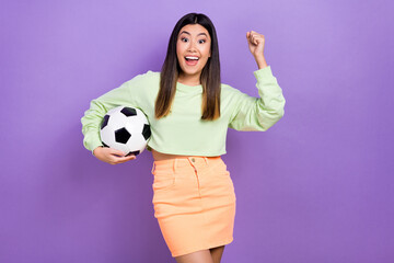 Photo of shiny lucky girl dressed green sweatshirt rising fist holding football ball isolated violet color background