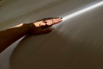 Hand placed on a sun ray light on the bed sheets. - 625888880