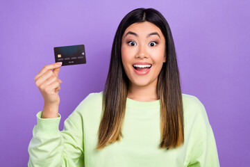 Photo of positive impressed woman dressed green clothes hold debit card spend money in online store isolated on purple color background