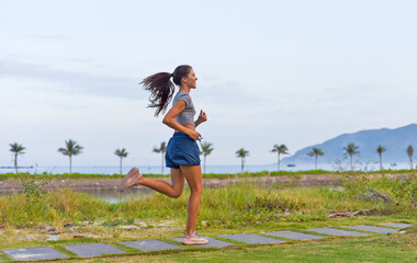 Young slim woman running  doing and sport exercises against sunset and beach with palms