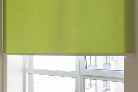 Details of green fabric roller blinds. Automatic curtain close-up on the window. Selective focus. Motorized shades. City outside the window.