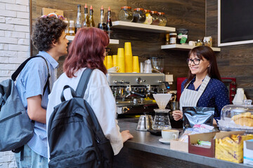 Customers of coffee shop making an order, talking to female barista cafe worker