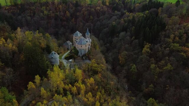 Old medieval castle with towers surrounded by deep woodland, aerial orbit view