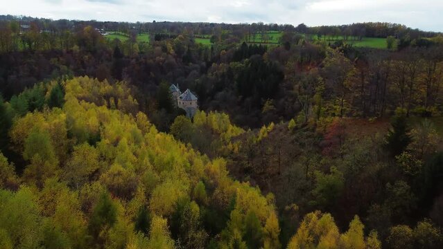 Castle tower hiding between trees of autumn forest, aerial drone view
