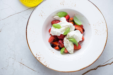 Beige plate with torn mozzarella, balsamic strawberries and green basil, high angle view on a white granite background, horizontal shot