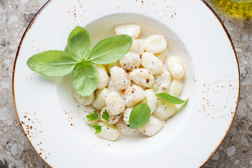 Middle close-up of potato gnocchi served with cheese sauce and green basil in a beige plate, above view, horizontal shot
