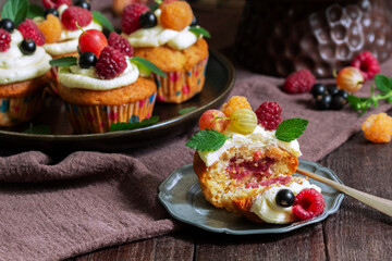 Cupcakes with butter cream and raspberry curd, decorated with berries on a wooden surface.