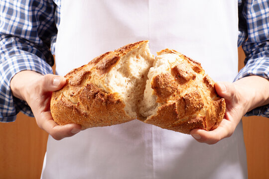 Manos de hombre partiendo un pan. Man's hands breaking bread.
