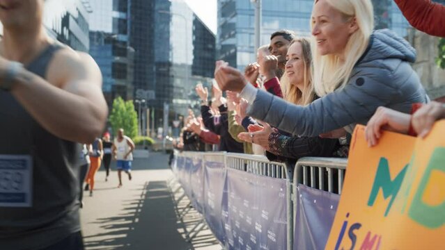 Slow Motion Portrait of a Male Marathon Runner Giving a High Five to Female Family Member in the Audience While Running. Middle Aged Wife Supporting her Husband in a Charity City Marathon Race
