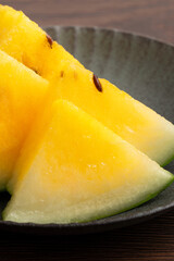 Sliced yellow watermelon in a plate on wooden table background.