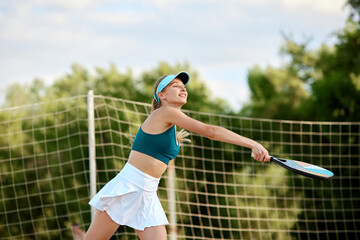 Young woman standing on beach, playing paddle tennis on warm summer day outdoors. Healthy lifestyle. Concept of sport, leisure time, active lifestyle, hobby, game, summertime, ad