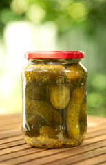 Salted, pickled cucumbers in a jar on a wooden table in the garden. Preservation, conservation. Background, copy space. Sunny bright day.