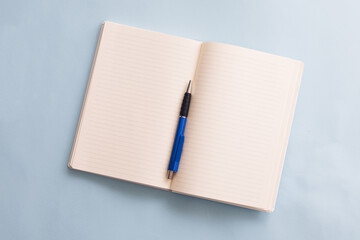 Top view of open empty notes and blue pen on blue background. School or office background ideas.