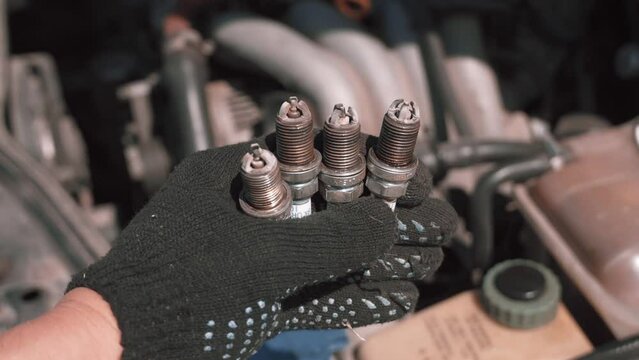 Spark plug. Master's hand shows to camera four candles used with soot and plaque, because of which engine was not produced or badly worked. Gasoline candles. Troubleshooting and troubleshooting.