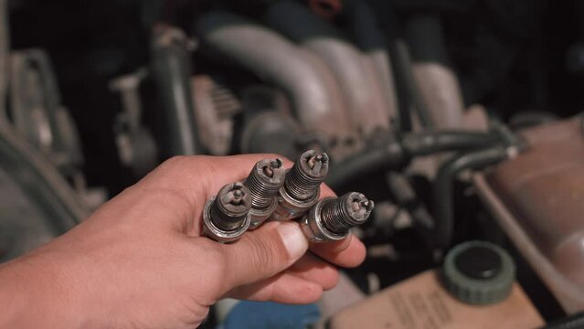 Spark plug. Master's hand shows to camera four candles used with soot and plaque, because of which engine was not produced or badly worked. Gasoline candles. Troubleshooting and troubleshooting.
