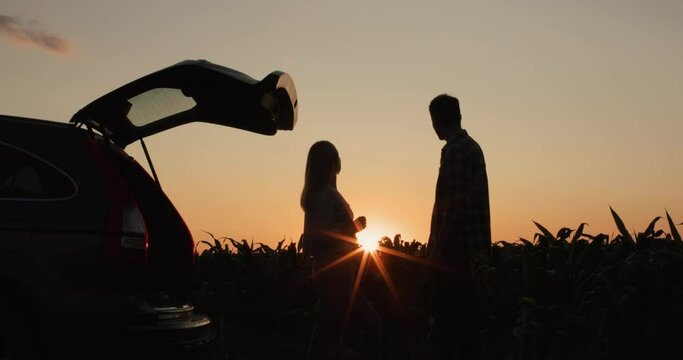 A young couple admires the sunset over the field, standing near their car