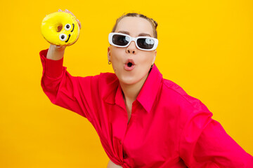 Cheerful pregnant woman holding a sweet yellow donut in her hand on a yellow background. Expecting a child, pregnancy and motherhood. The concept of healthy and unhealthy food, diet. Junk food