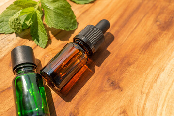 Brown and green bottles of essential oils. natural cosmetics for skin care. A bottle and fresh mint on a wooden table. Taking care of health and beauty.