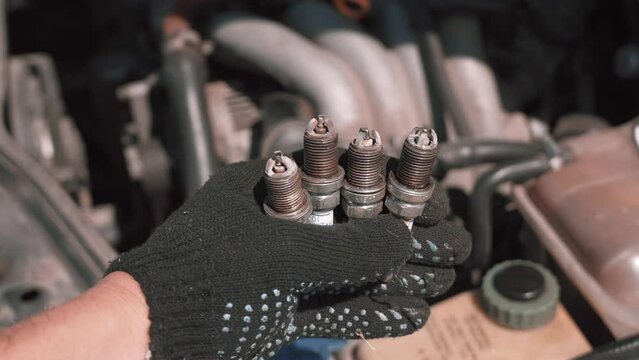 Spark plug. Master's hand shows to camera four candles used with soot and plaque, because of which engine was not produced or badly worked. Gasoline candles. Troubleshooting and troubleshooting.
