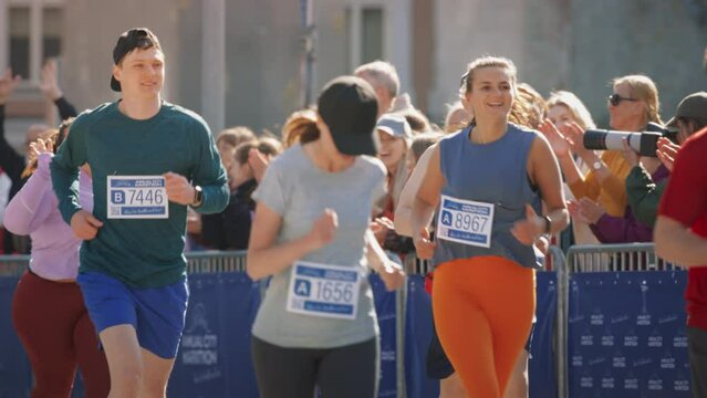 Slow Motion Portrait of a Group of People Participating in a Marathon and Running Through a City Trail. Joggers Giving their Best to Achieve the Finish Line, with Audience Cheering for Them