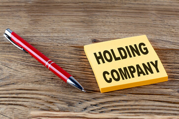 HOLDING COMPANY text on sticky with pen on the wooden background